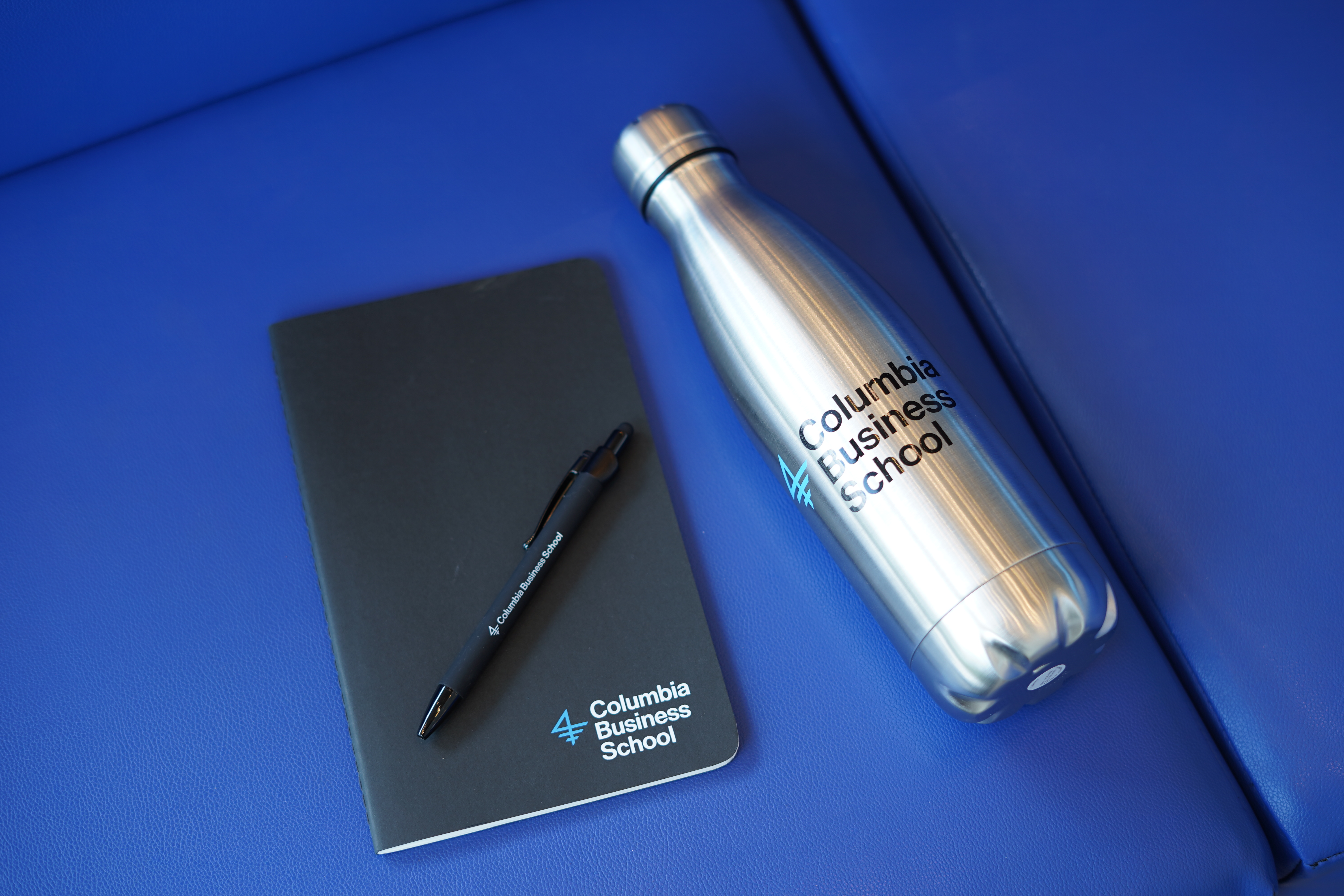 A CBS-branded notebook, pen, and water bottle sit on a bright blue couch cushion
