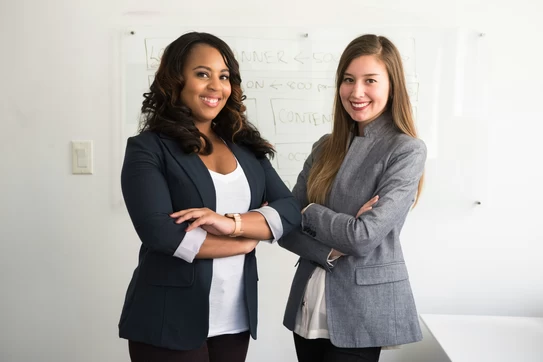Two women in suits standing beside wall photo. Photo by Christina @ wocintechchat.com on Unsplash.