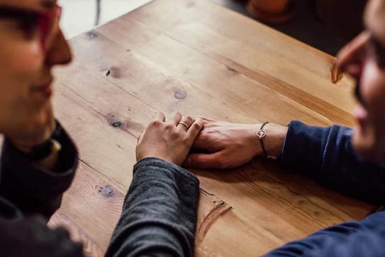 Two people sitting together at a table, holding hands