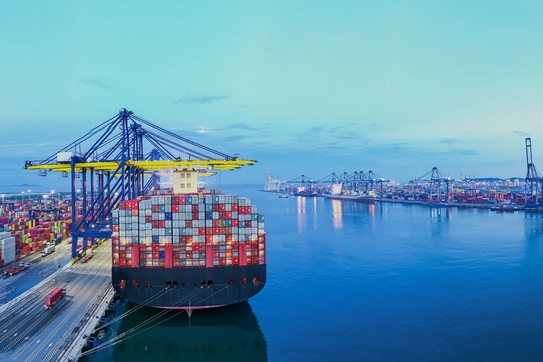 A shipping container ship at a port being unloaded by gantry operators