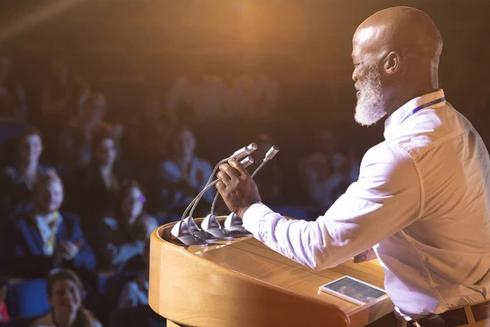 A dressed-up speaker at a podium addresses an audience