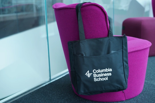 A black CBS-branded tote bag hangs off a fuschia easy chair